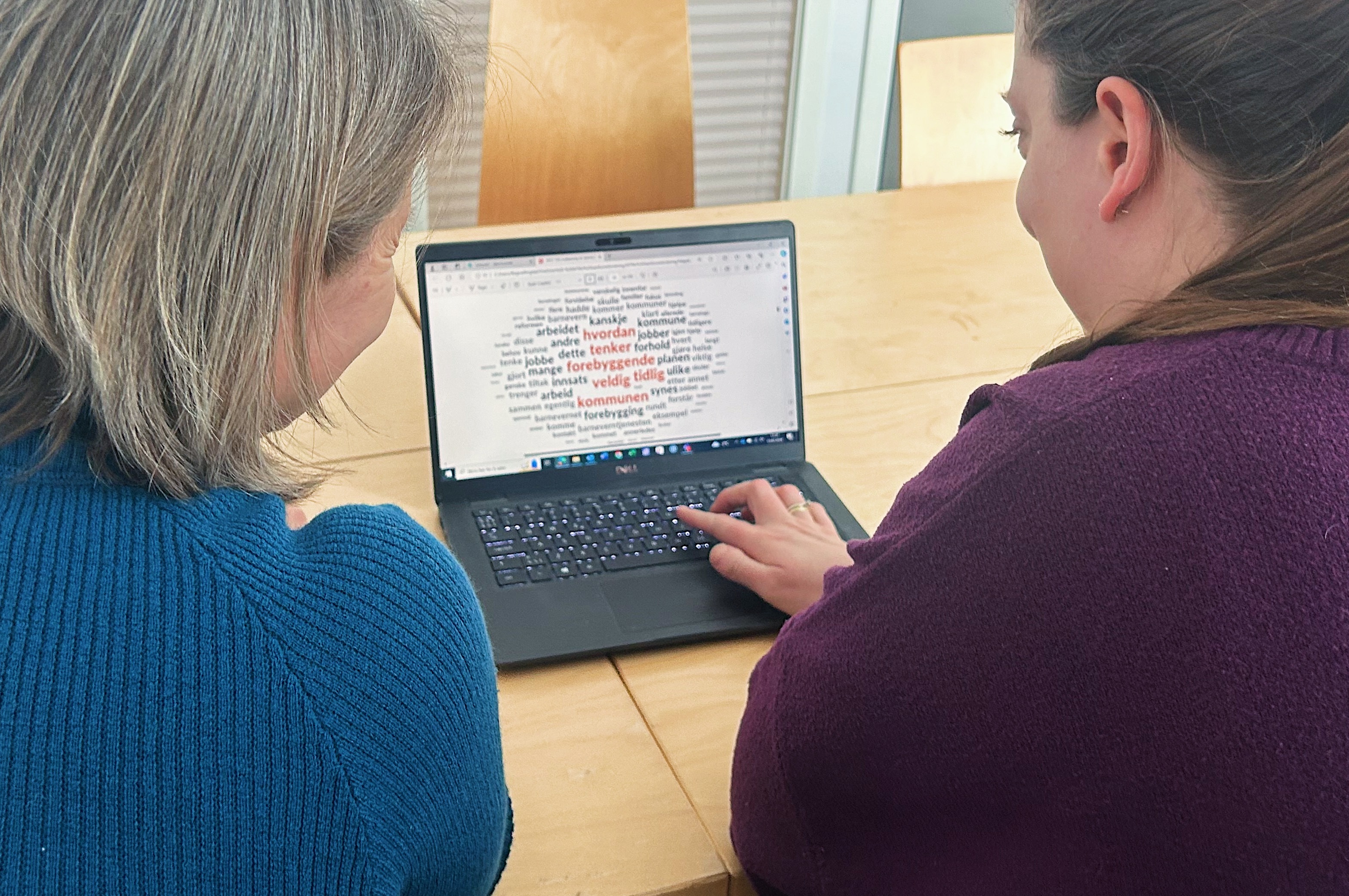 Lena Westby og Regine Ringdal sitter foran en PC som viser en ordsky. I ordskyen er ordene "Hvordan tenker forbyggende veldig tidlig kommunen" markert i rødt. Fotografi.